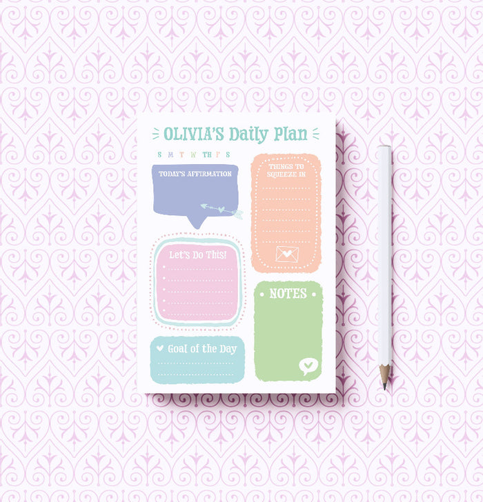 A photo of a Daily Gratitude Notepad with its cover design visible, along with a pen, against a patterned background.