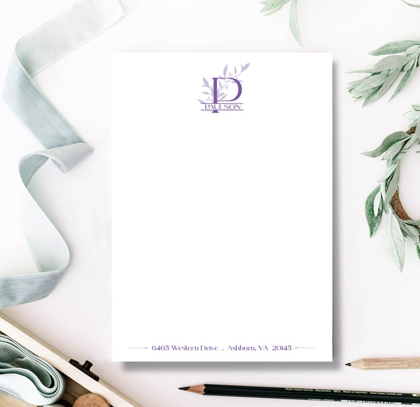Notebook with a decorative cover featuring a logo and text, surrounded by stationery items on a white background.