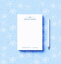 A personalized notepad with a blue patterned background, featuring a monogram that reads 'Abigail Moore'. The notepad is accompanied by a white pen.